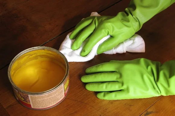 Person trägt gelbe Politur mit Tuch auf Holztisch auf